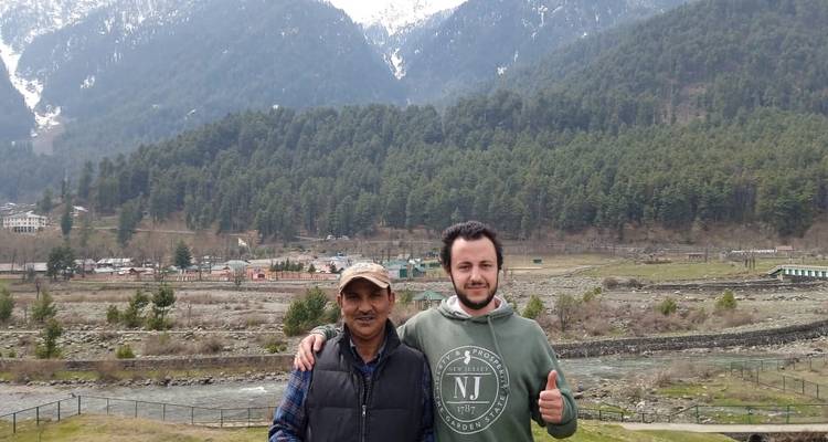 Deux personnes posant devant des montagnes enneigées et une rivière.