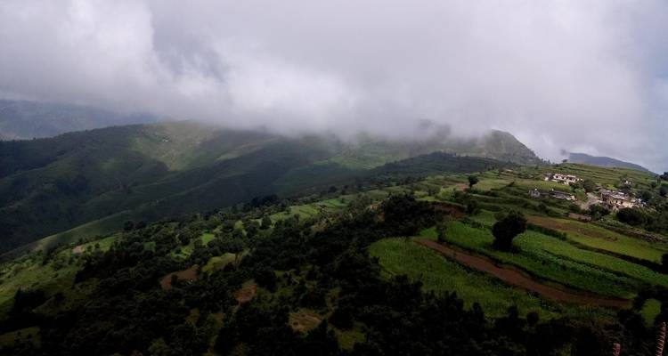 A scenic view of green hills and a rural landscape under cloudy skies.