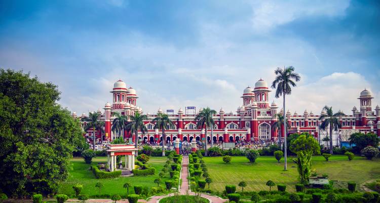Un edificio rojo histórico rodeado por un jardín bien cuidado.