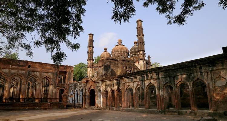 Una estructura antigua con cúpulas y arcos entre árboles.