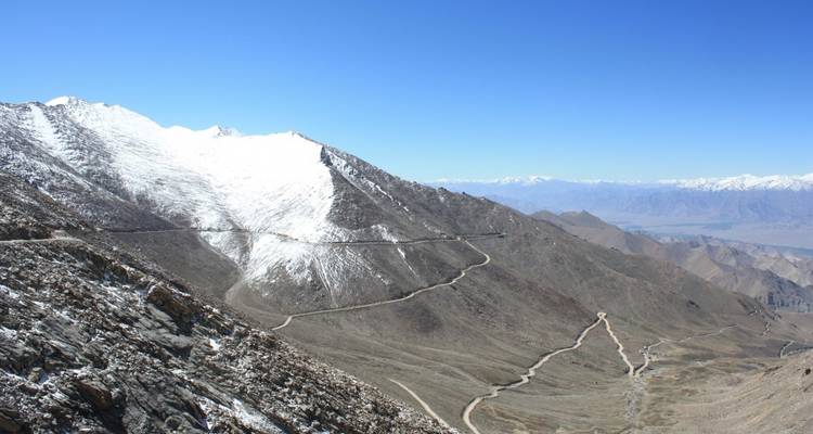 Gewundene Bergstraße mit schneebedeckten Gipfeln in der Ferne.