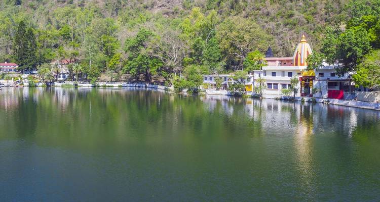 Lac avec des reflets de bâtiments de temple et d'arbres sur une colline.