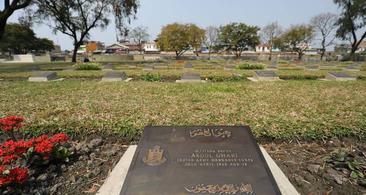 Grafsteen op een begraafplaats met bloemen en bomen eromheen.