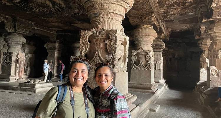 Dos mujeres de pie en una cueva tallada en roca con columnas ornamentadas.
