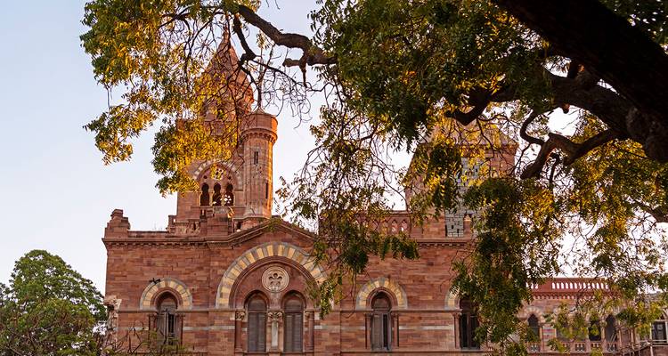 Rotes Sandsteingebäude, eingerahmt von Bäumen, zeigt historische Architektur.