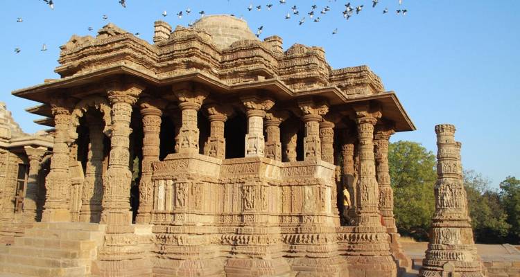 Temple avec des sculptures complexes et des oiseaux volant au-dessus, entouré d'arbres.