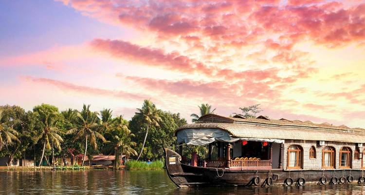 Traditional wooden houseboat cruises Kerala backwaters at sunset with palm trees and vibrant sky.