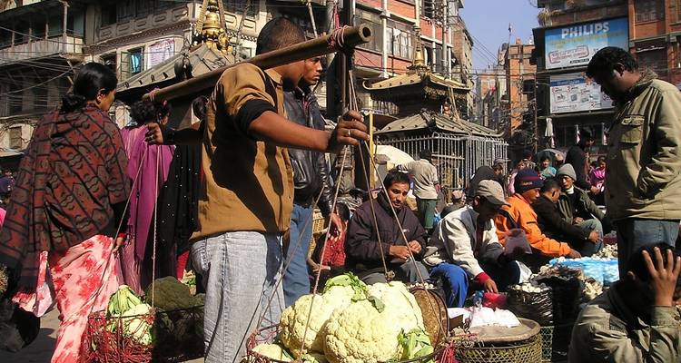 Escena bulliciosa del mercado al aire libre con vendedores vendiendo coliflor y productos entre edificios históricos.