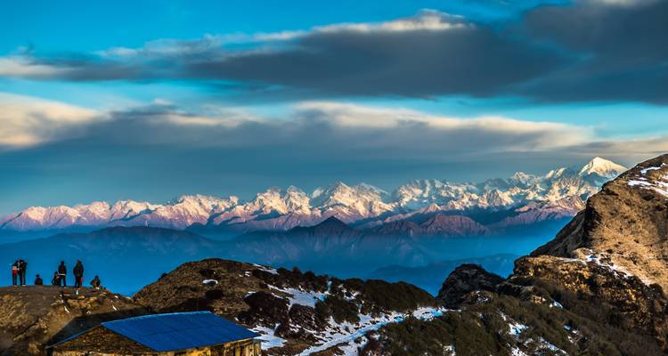Los picos del Himalaya cubiertos de nieve brillan en rosa al amanecer sobre una cresta rocosa con pequeños espectadores.