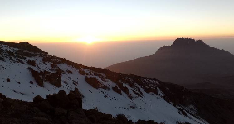 Sunrise over a mountainous horizon with snow in the foreground.