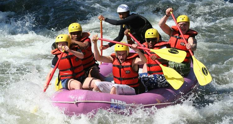 A group of rafters in a pink raft navigating a turbulent river.