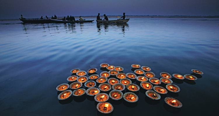 Floating lit diyas at dawn on a river.
