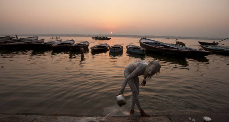 Sunrise at the river bank with boats and a person bathing.