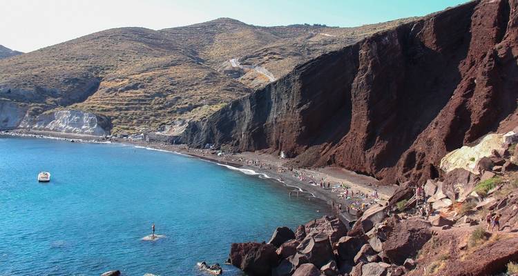 Un littoral spectaculaire avec une formation rocheuse volcanique rouge et une plage de sable.