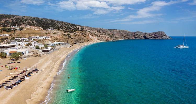 Long sandy beach with clear blue waters and scattered sun loungers.