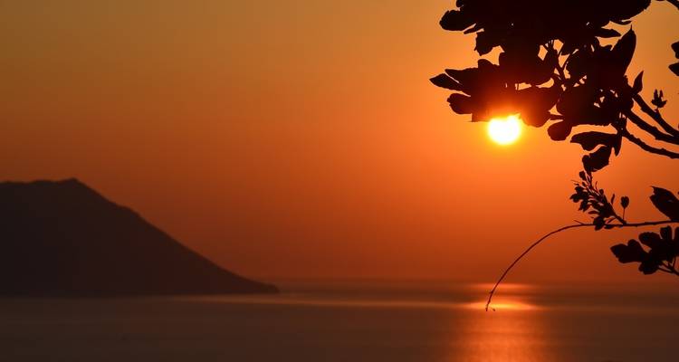 Ein lebendiger orangefarbener Sonnenuntergang über ruhigen Meeresgewässern und fernen Hügeln.