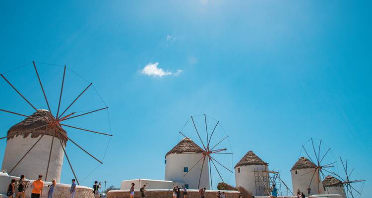 Des moulins à vent avec des touristes autour par une journée ensoleillée en Grèce.