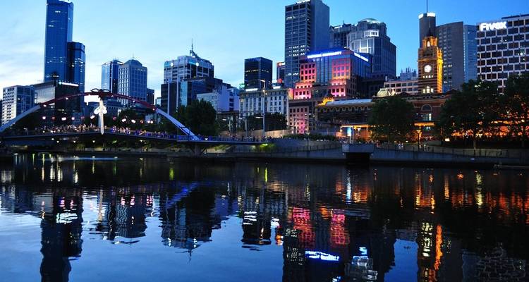 Stadsskyline 's nachts met verlichte gebouwen die reflecteren op een rivier.