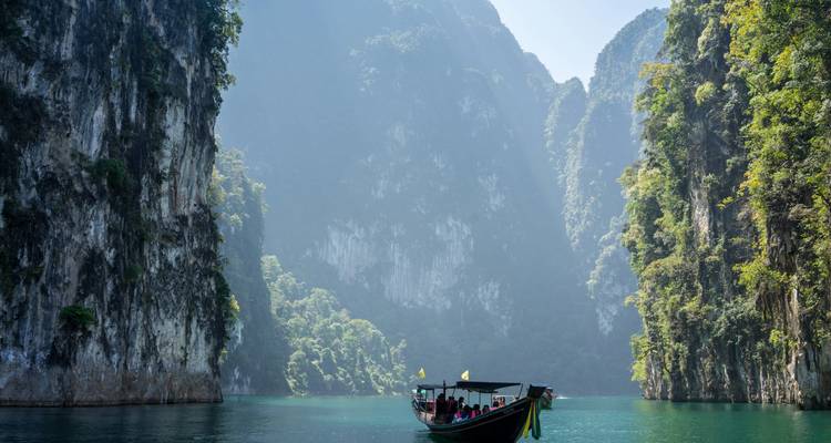 Long-tail boat glides through jade waters between soaring limestone cliffs.