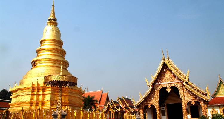 Golden chedi and ornate viharn of a northern Thai temple complex under clear skies.