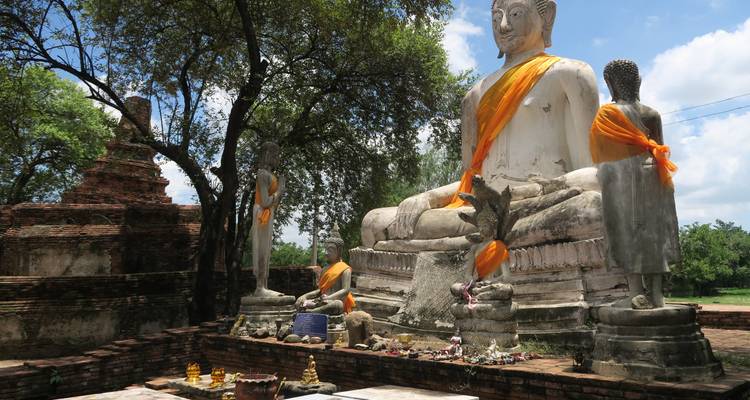 Large seated Buddha draped in saffron cloth amidst ruined brick chedis and trees.