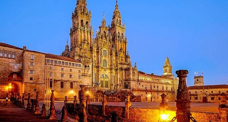De verlichte gevel van de kathedraal van Santiago de Compostela gloeit tijdens het blauwe uur boven een leeg stenen plein.