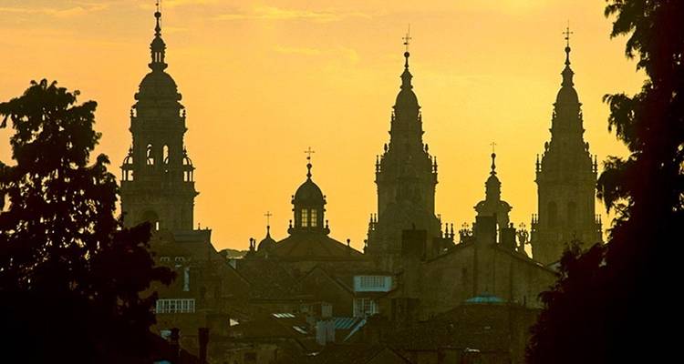 De torenspitsen van de Kathedraal van Santiago de Compostela steken donker af tegen een gouden zonsonderganghemel.