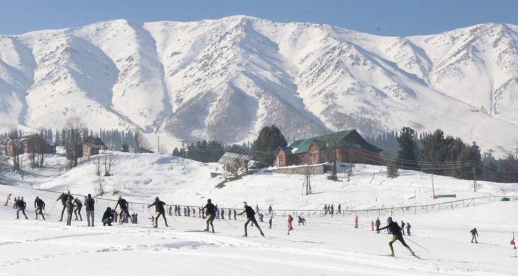 Menschen, die auf einem verschneiten Hügel Ski fahren, mit Bergen im Hintergrund.