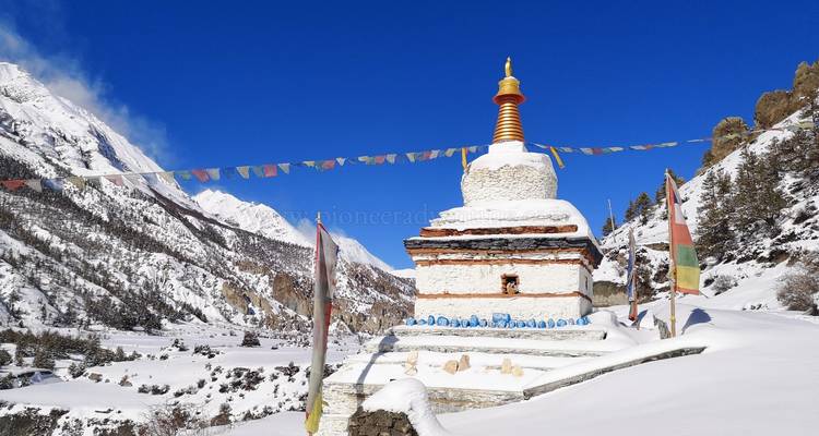 Estupa cubierta de nieve con banderas de oración contra un telón de fondo montañoso.