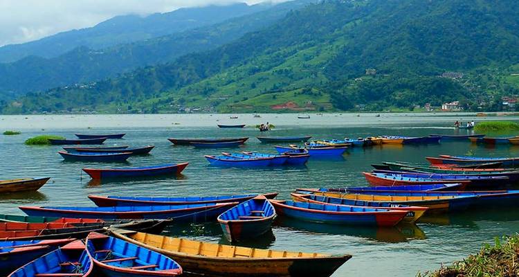 Kleurrijke boten drijvend op een meer omringd door weelderige heuvels in Pokhara, Nepal.