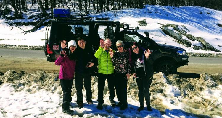 A group posing happily in front of a vehicle on a snowy mountain road.