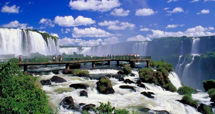 Visitantes en un paseo marítimo con vista a las Cataratas del Iguazú con exuberante vegetación circundante.