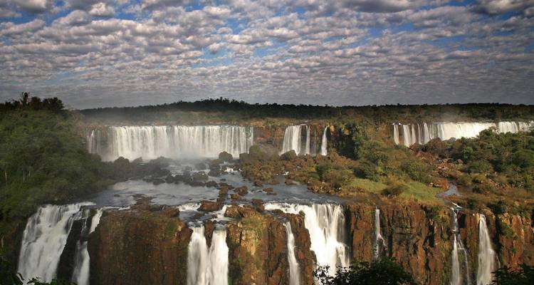 Vista panorámica de las Cataratas del Iguazú con nubes dramáticas y áreas boscosas.