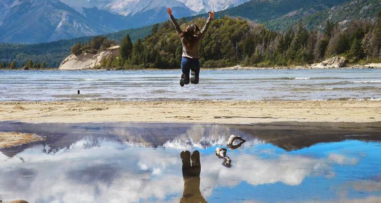 Personne sautant joyeusement sur une plage avec des montagnes au loin.