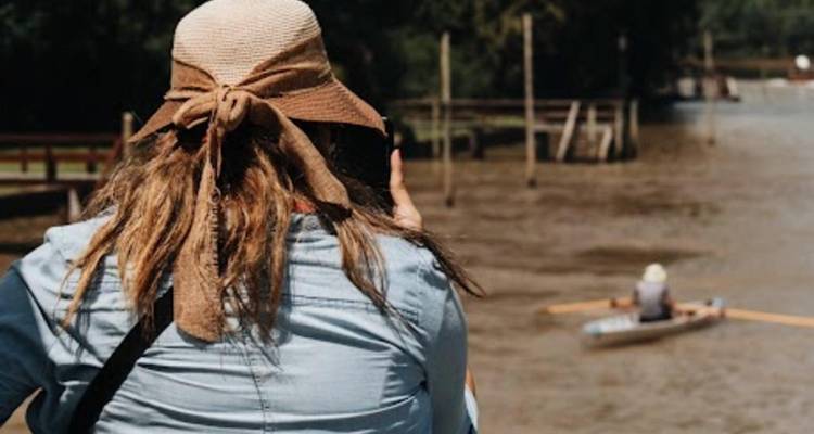 Femme prenant une photo au bord de la rivière avec un rameur en arrière-plan.