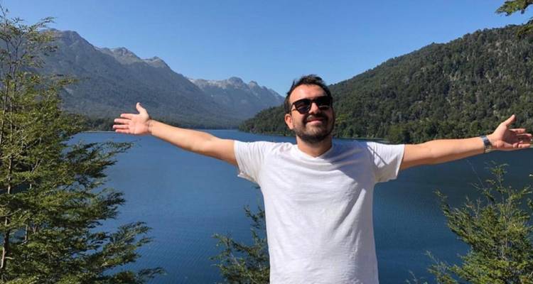 Homme posant joyeusement devant un lac de montagne pittoresque.