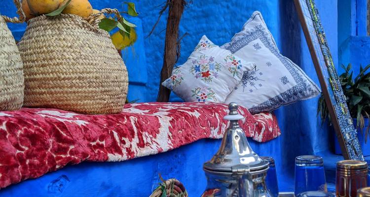 Nature morte colorée de paniers tissés, de coussins brodés et d'une théière en argent sur un mur bleu.