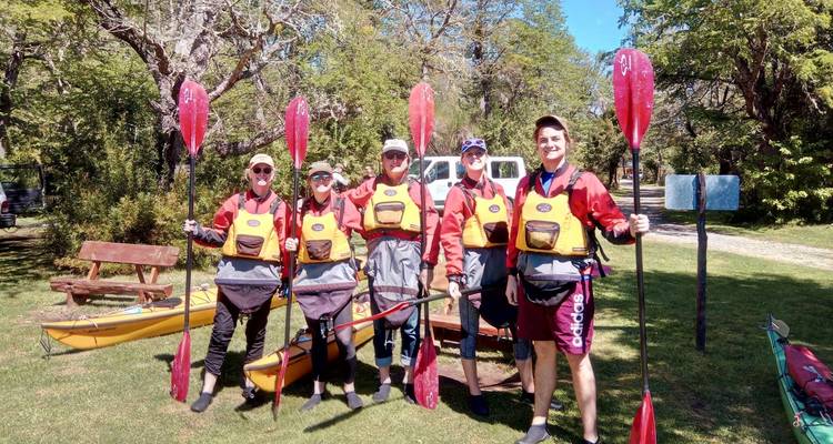 Grupo de personas con equipo de kayak posando con remos, rodeados de vegetación.