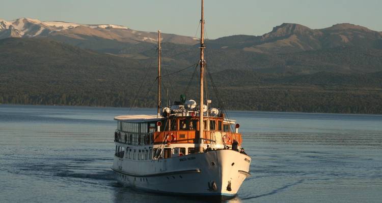 Un barco clásico navegando en un lago tranquilo con montañas al fondo.