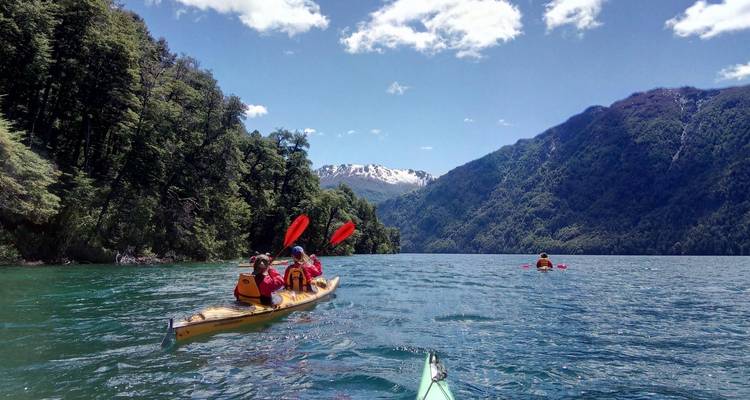 Personas navegando en kayak en un lago pintoresco rodeado de colinas boscosas y montañas.