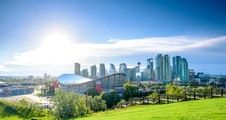 Horizonte soleado de Calgary con la arena Saddle-dome y modernos rascacielos elevándose sobre un parque verde.