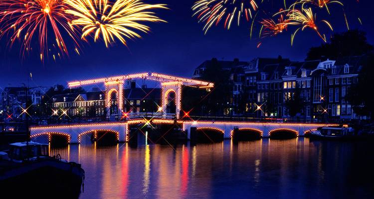 Vibrant fireworks burst above Amsterdam’s illuminated Magere Brug reflecting on the tranquil canal at night