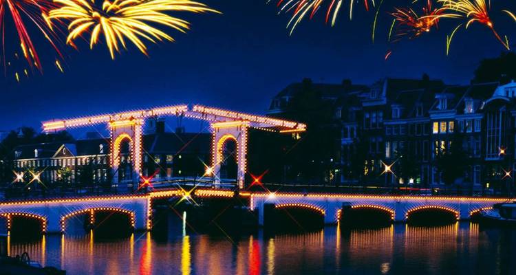 Les feux d'artifice éclatent au-dessus du Magere Brug illuminé d'Amsterdam tandis qu'il se reflète sur un canal tranquille la nuit.