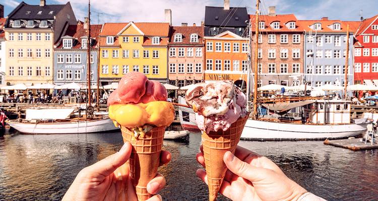 Deux cônes de glace colorés sont tenus devant le port de Nyhavn à Copenhague en arrière-plan.