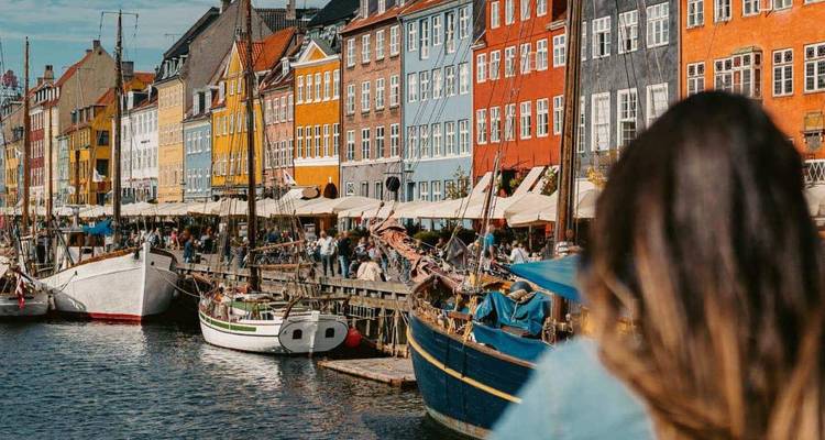 Lebhafte Fassaden und historische Segelboote spiegeln sich im Nyhavn-Kanal von Kopenhagen wider, während ein Besucher die Aussicht bewundert.