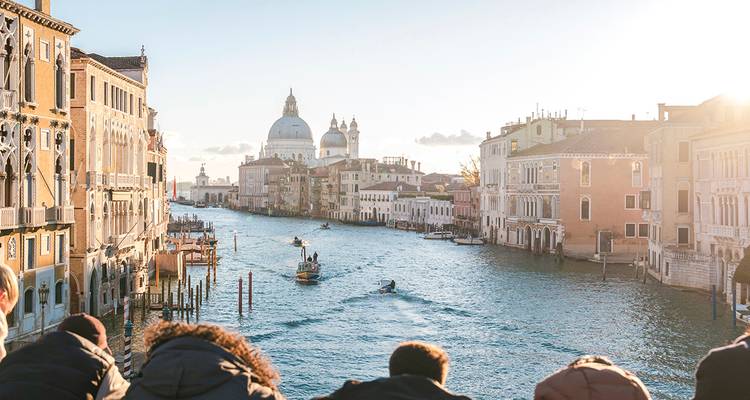 View down Venice’s Grand Canal with domes, gondolas and onlookers leaning over a bridge.