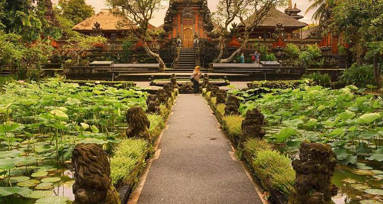 Estanque lleno de lotos conduce a un pabellón de templo balinés ornamentado rodeado de exuberante vegetación.