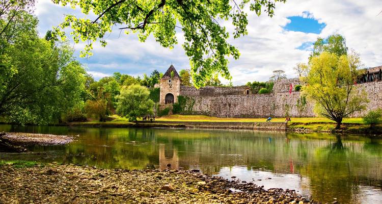 Château historique au bord d'une rivière entouré d'une végétation luxuriante.