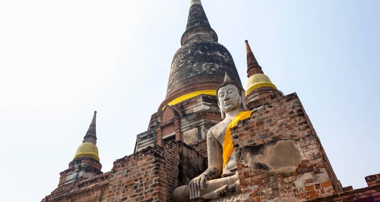 Antigua estupa de ladrillo con estatua de Buda sentado cubierta con tela amarilla en el parque histórico de Ayutthaya.