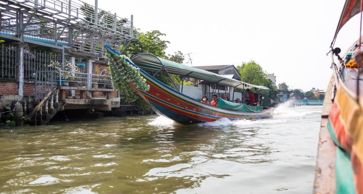 Bote de cola larga colorido acelerando por un canal de Bangkok salpicando agua.